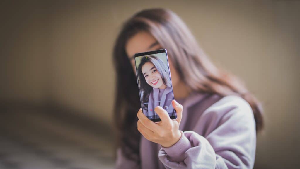Young woman holding up phone to take a video in selfie mode